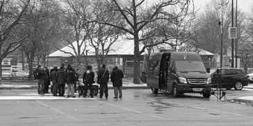 Film crew working outdoors in snowy weather next to a black van.