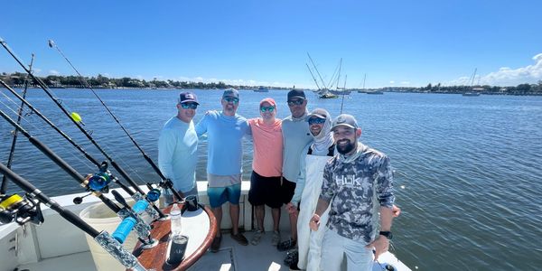 Six friends posing on a fishing boat under clear blue skies.