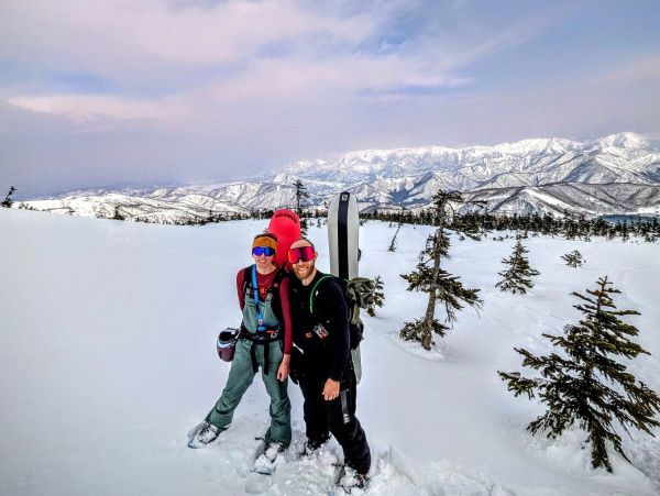 Two people posing on a snowy mountain with snowboards.