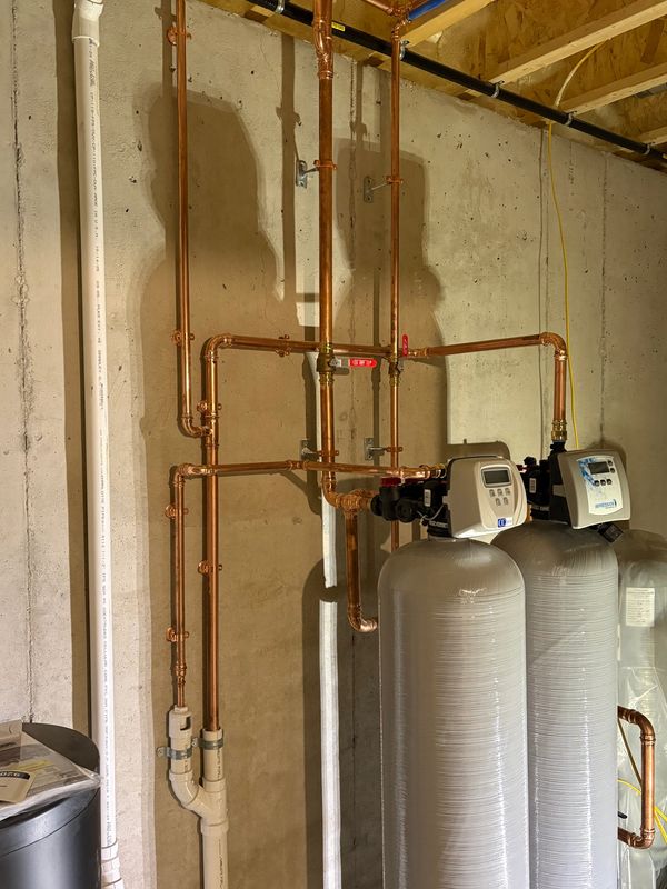 Copper piping connected to two large water treatment tanks in a basement.