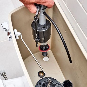 Hand repairing or inspecting a toilet tank mechanism.