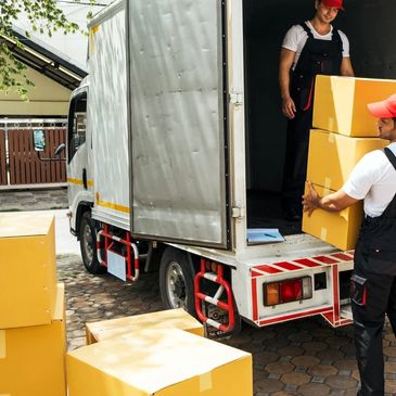 Two movers in uniforms loading yellow boxes into a truck.