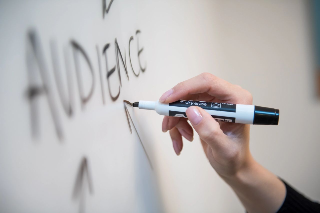 Woman's hand writing the word audience on a whiteboard, with arrows