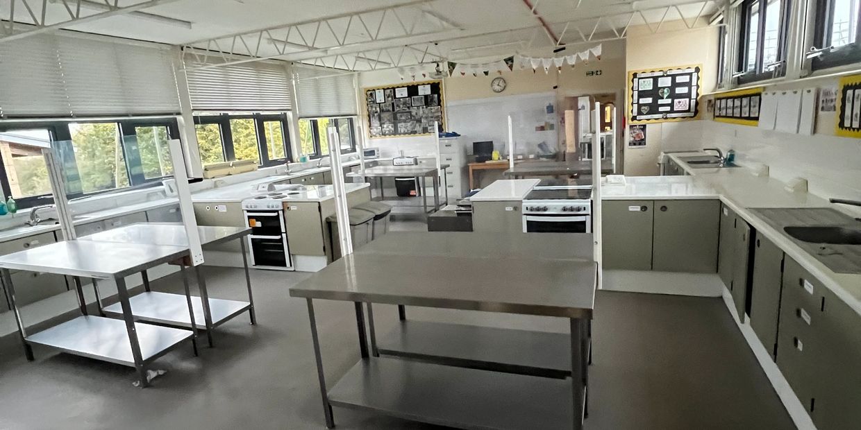 Empty classroom kitchen with stainless steel tables and ovens.