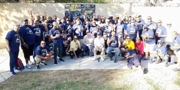 Large group photo of people in blue shirts outdoors.