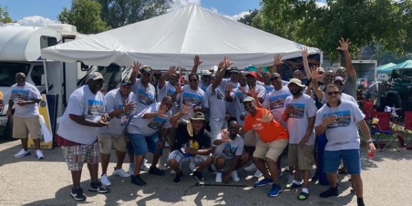 Group of people posing cheerfully outdoors under a tent.