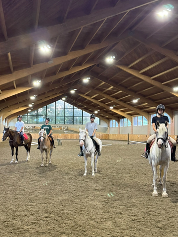 Four children standing next to a brown and white horse inside a stable.
