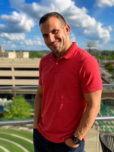 Man in red polo shirt smiling outdoors on a sunny day.