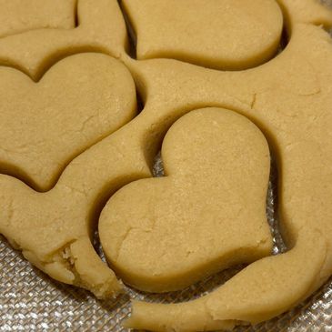 Heart-shaped cookies cut out from dough on a baking mat.
