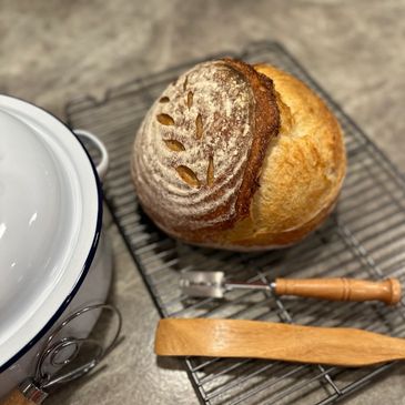 Freshly baked artisan bread cooling on a wire rack beside baking tools and a Dutch oven.