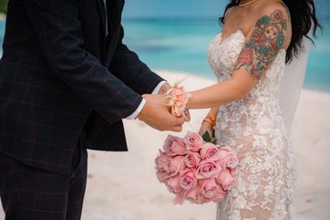 Bride and groom holding hands with pink roses on a beach wedding.