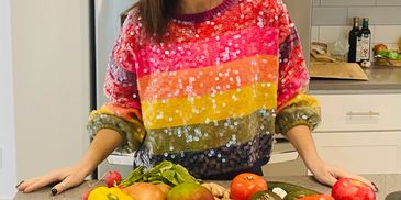 Person wearing a colorful sequined sweater standing behind a kitchen counter with fresh vegetables.