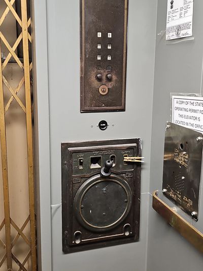 Vintage elevator control panel with a large circular dial and metal gate.