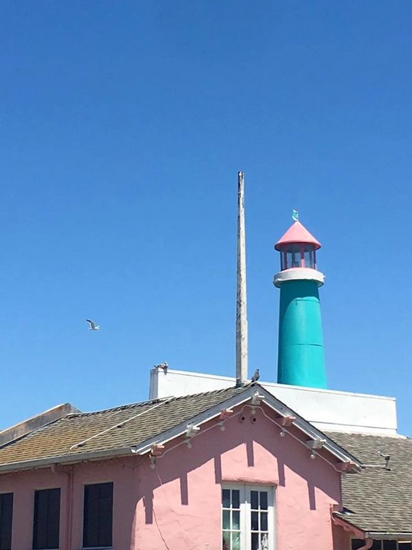 Colorful lighthouse and pink building under clear blue sky.