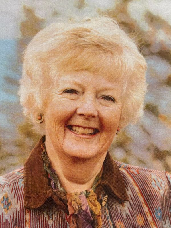 Smiling elderly woman with light hair and patterned clothing.