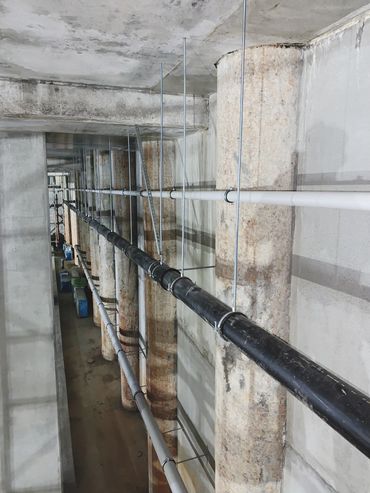Concrete pillars with suspended pipes in an industrial basement.