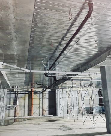 Interior of an unfinished building with exposed pipes and scaffolding.