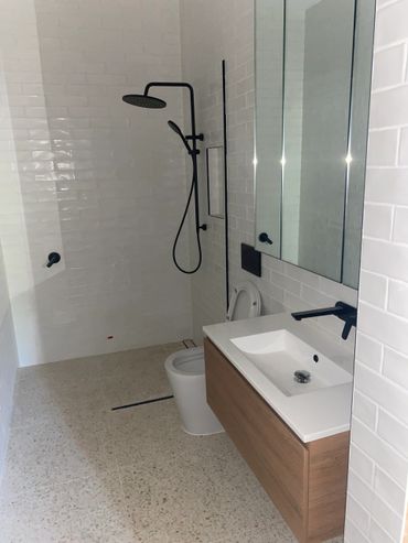 Modern bathroom with black fixtures, white tiles, and wooden vanity.