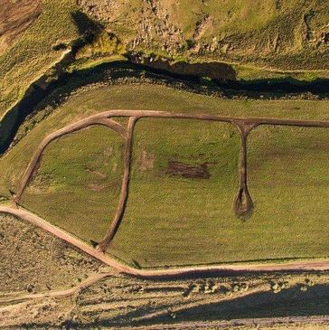 Aerial view of a green field with dirt paths and a small stream.