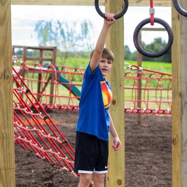 Boy playing on playground rings outdoors wearing a blue shirt.