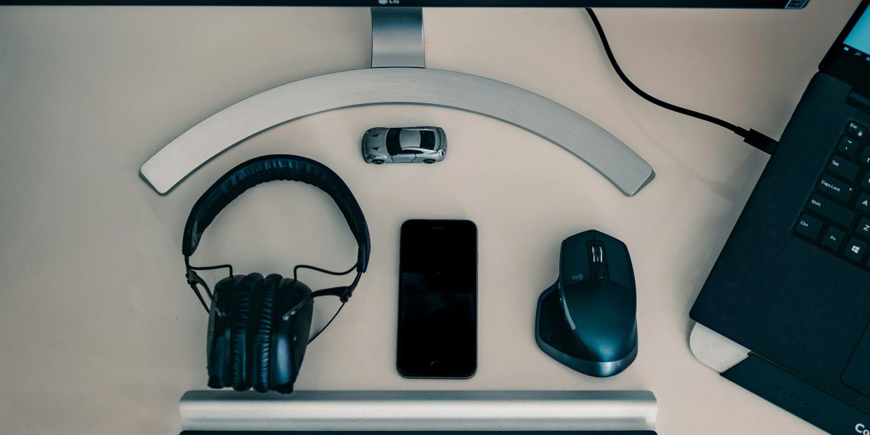 Tech essentials: headphones, smartphone, mouse, and a laptop on a desk.