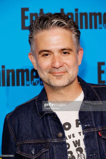 Man smiling in front of an Entertainment Weekly backdrop.