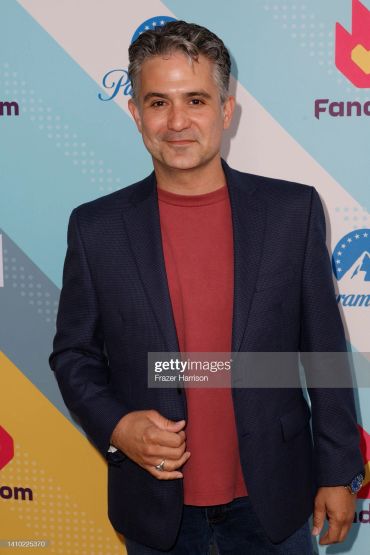 Man in a navy blazer and red shirt posing confidently.