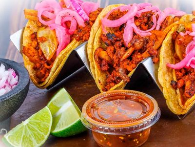 Three tacos with meat, pickled onions, and lime wedges.