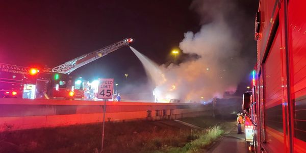 Firefighters extinguishing a nighttime fire on a highway.