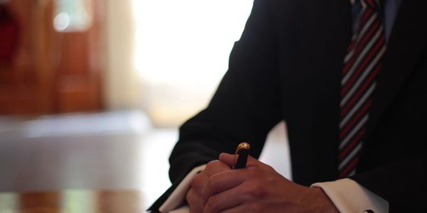 Manos con bolígrafo y traje formal escribiendo.