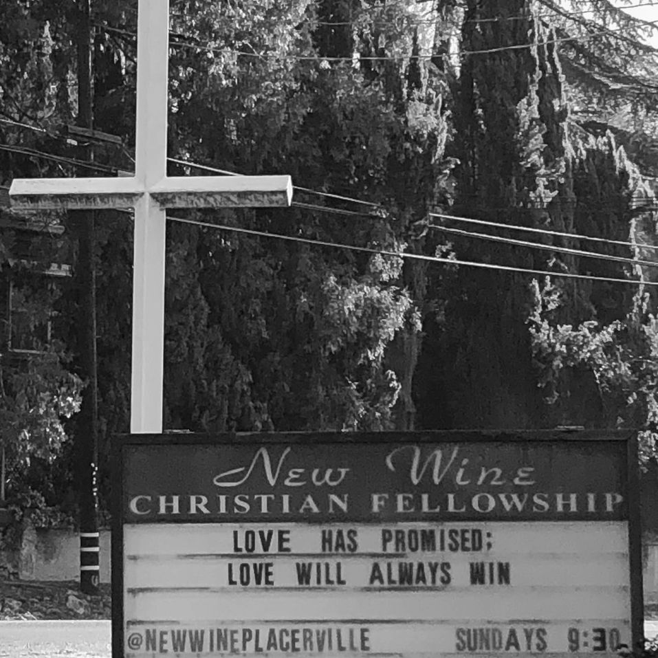 Church sign with message about love and a white cross behind it.