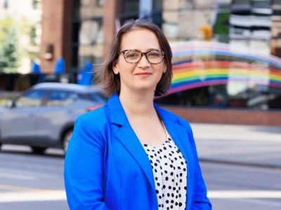 Woman in blue blazer standing outdoors with a confident smile.