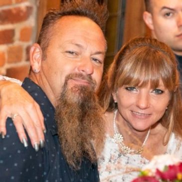 A group of people enjoying a social gathering with flowers and warm brick walls.