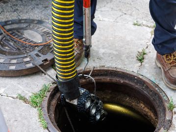 Worker cleaning a sewer with a robotic device.