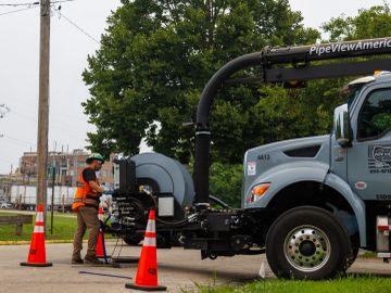 Worker operating sewer inspection truck with safety cones.