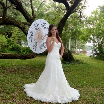 Bride in a white lace wedding gown holding a parasol outdoors.