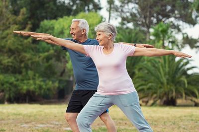 Elderly couple practicing yoga outdoors in a park.