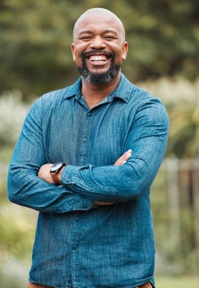 Smiling man in a blue shirt with arms crossed outdoors.