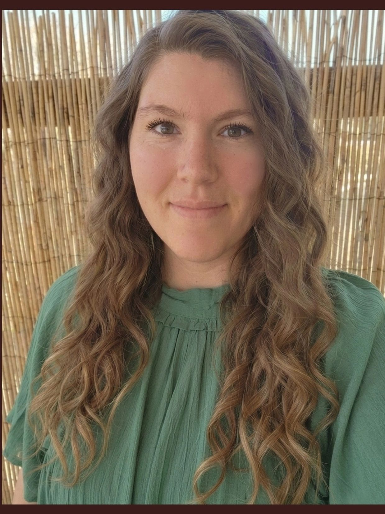 Woman with long curly hair wearing a green blouse against a bamboo background.