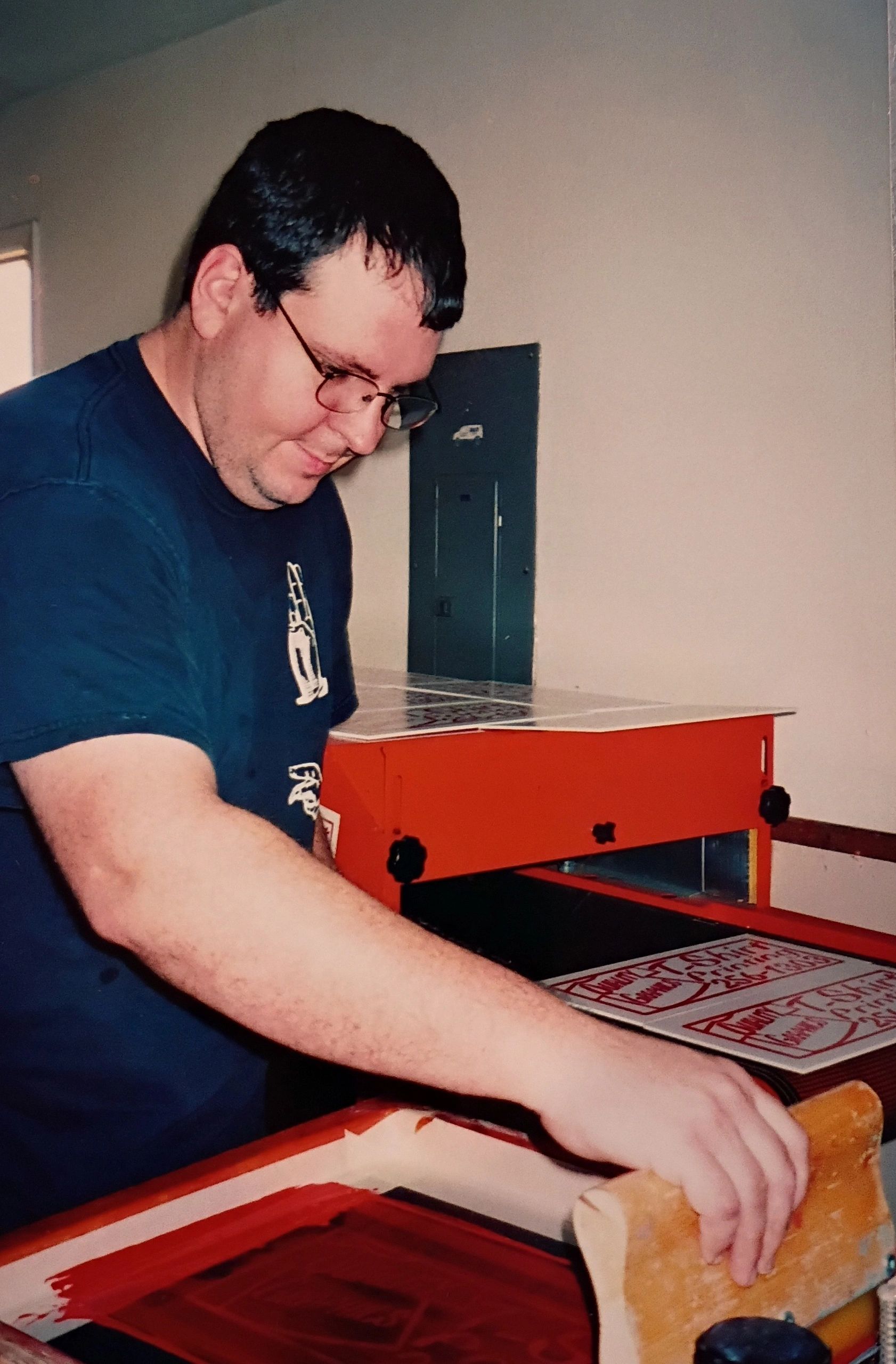 Man screen printing with a wooden squeegee on a red ink screen.