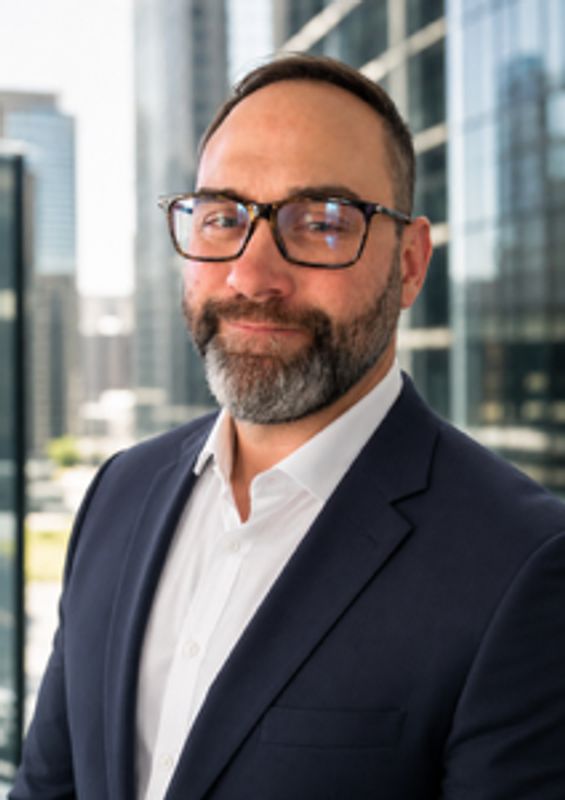 Man with glasses in a suit smiling confidently.