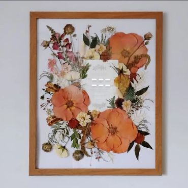 A framed artwork with large orange flowers and smaller blooms.