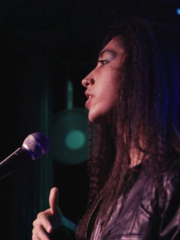 Person speaking into a microphone on stage with focused expression.