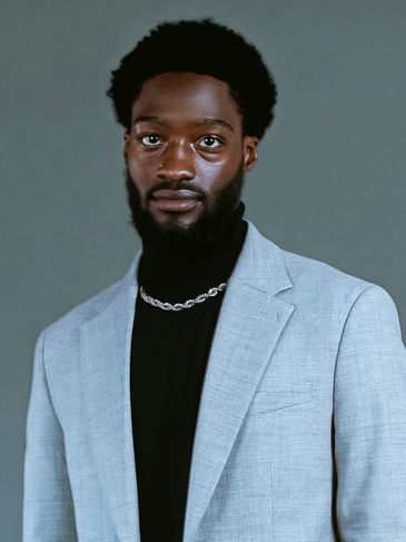 Portrait of a man in a light gray blazer and black shirt.