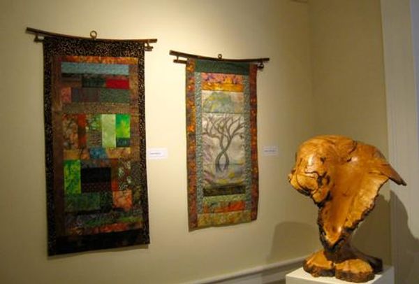 Two framed tapestries hang on a wall next to a light-colored wooden sculpture