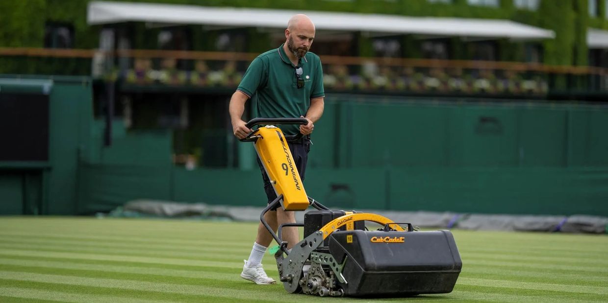 LawnDNA owner Andy Dawson operating a yellow lawn mower on a tennis court at Wimbledon AELTC
