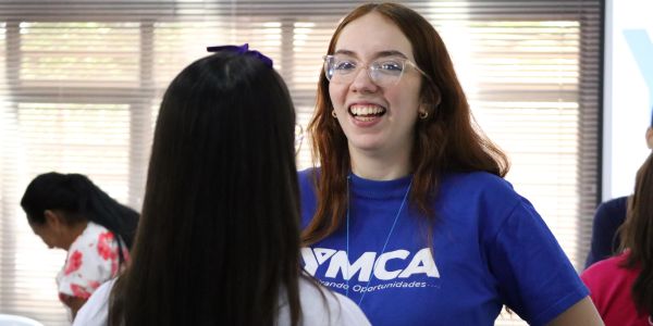 Two women engaged in a friendly conversation indoors, one wearing a blue YMCA shirt.
