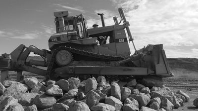 Bulldozer on rocky terrain under cloudy sky.