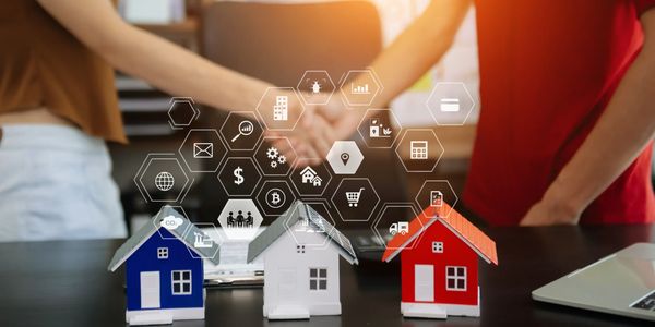 Two people shaking hands over small house models with digital icons representing real estate concepts.