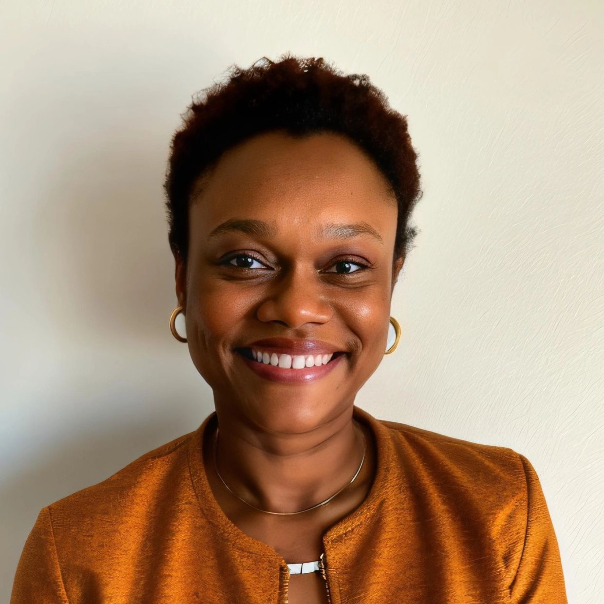 Smiling woman with short curly hair wearing a burnt orange top and gold earrings.